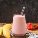 pink smoothie in glass next to bananas and strawberries