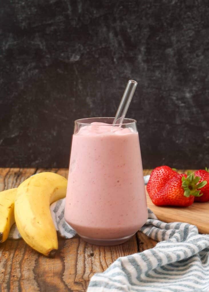 pink smoothie in glass next to bananas and strawberries 