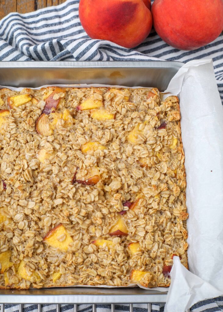 Baked Peach Oatmeal in metal pan with striped towel