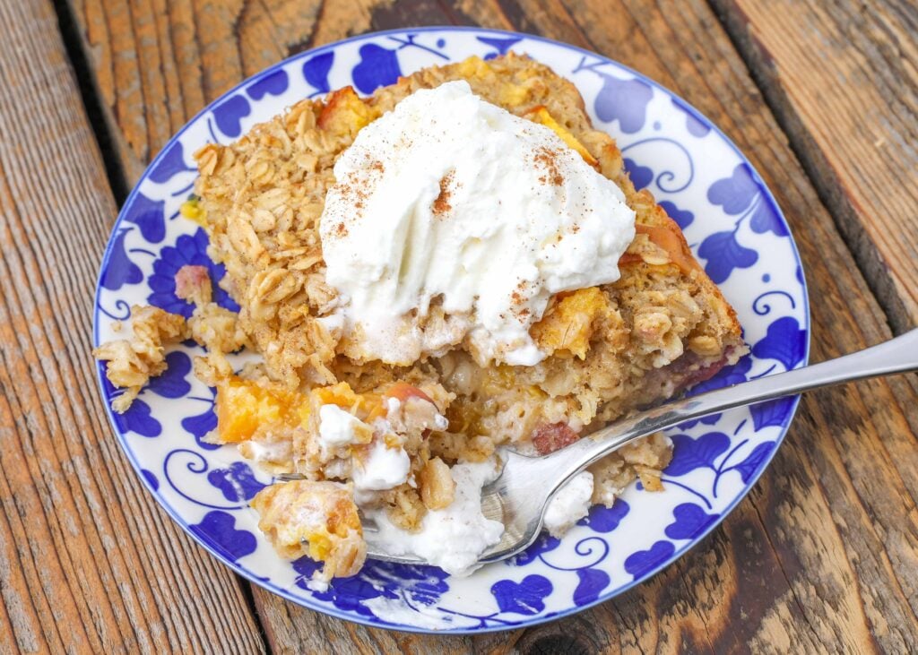 Peach Baked Oatmeal with whipped cream on top on a small blue plate