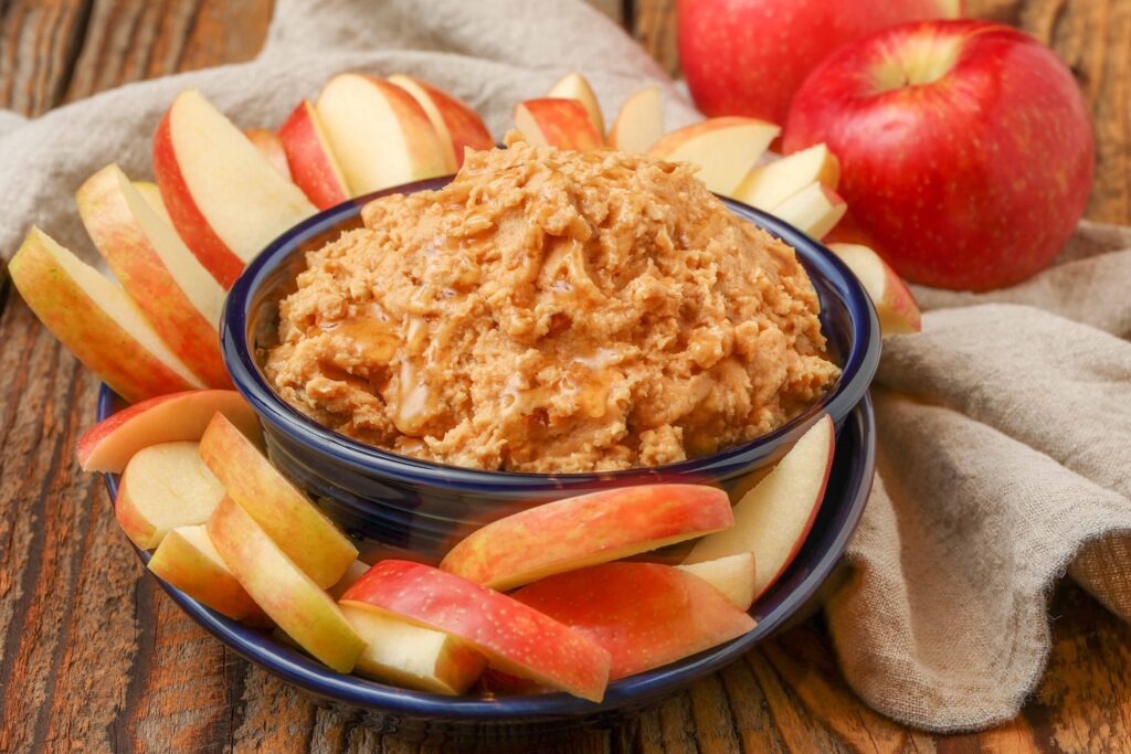 peanut butter dip in blue bowl with apples around it