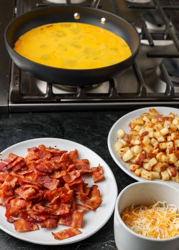 eggs, bacon, shredded cheese, and potatoes next to stove