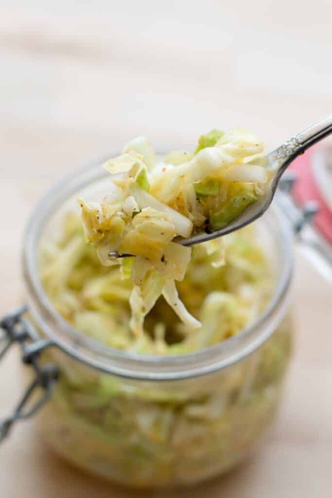 A bowl of food on a plate, with Cabbage and Coleslaw