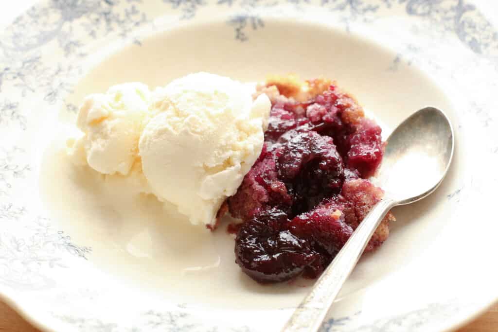 A close up of food on a plate, with Cherry and Ice cream