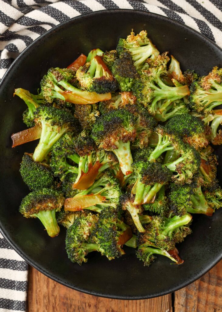roasted broccoli in black bowl with black and white towel