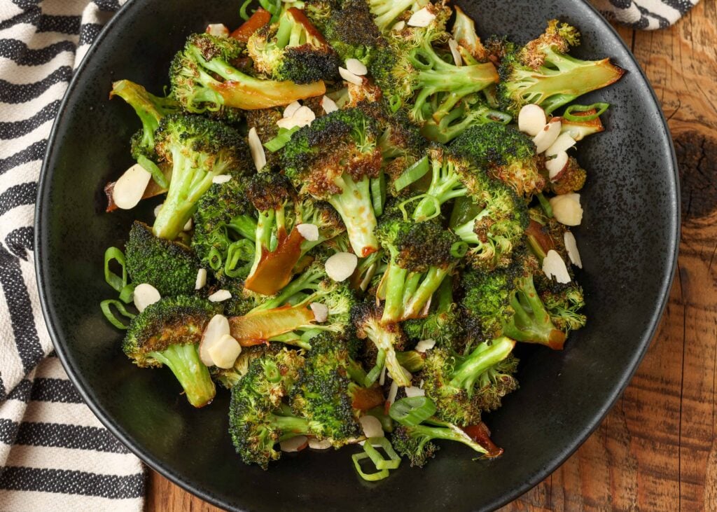roasted broccoli in black bowl with striped napkin