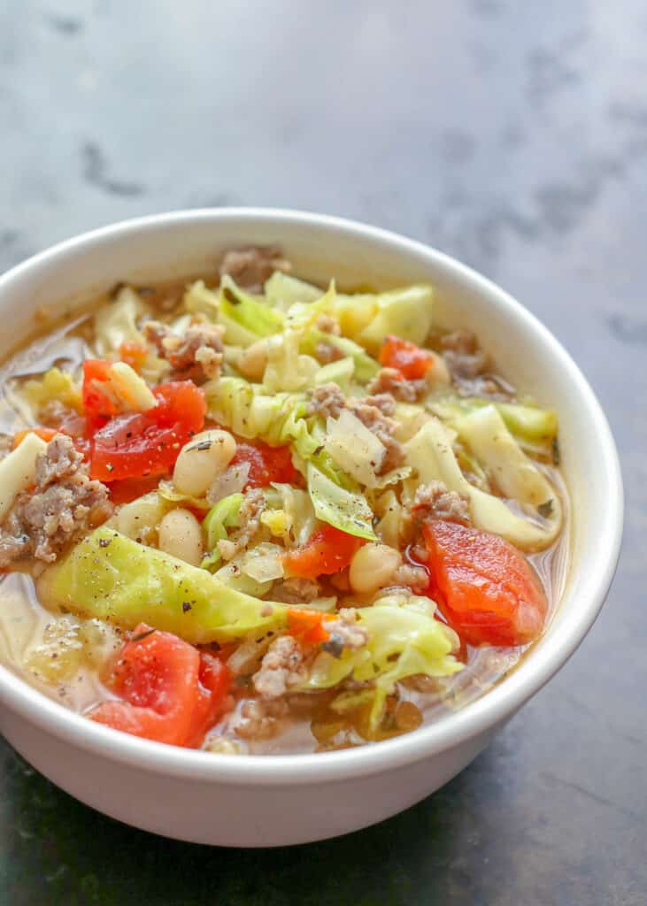 White beans and cabbage with sausage in bowl on gray table