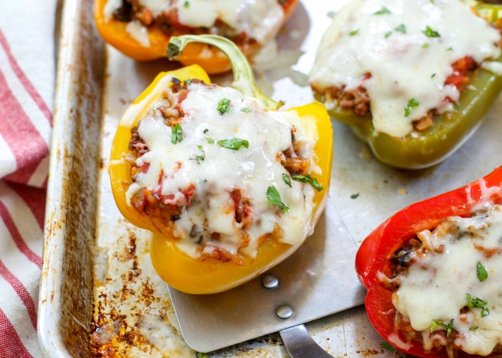 Peppers stuffed with rice and ground beef on a baking tray with a spatula