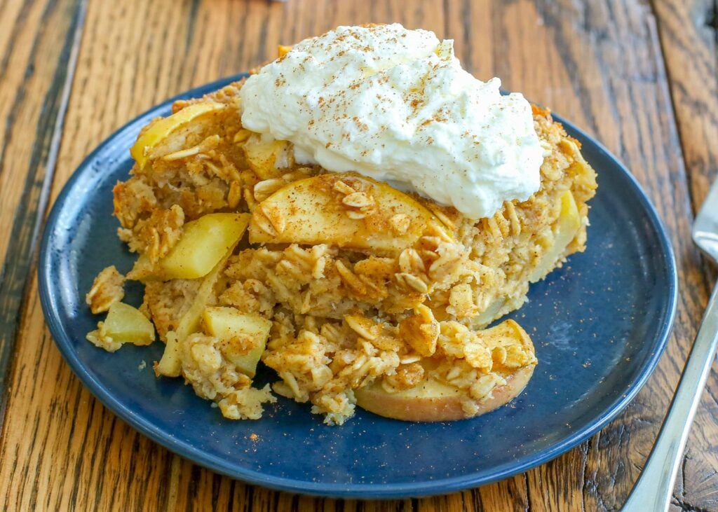 baked oatmeal with apples, whipped cream on top, on blue plate