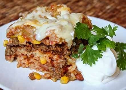 sliced Mexican Lasagna on white plate with sour cream and cilantro