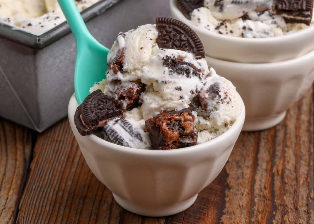 vanilla ice cream with brownies in a small white bowl with a teal spoon