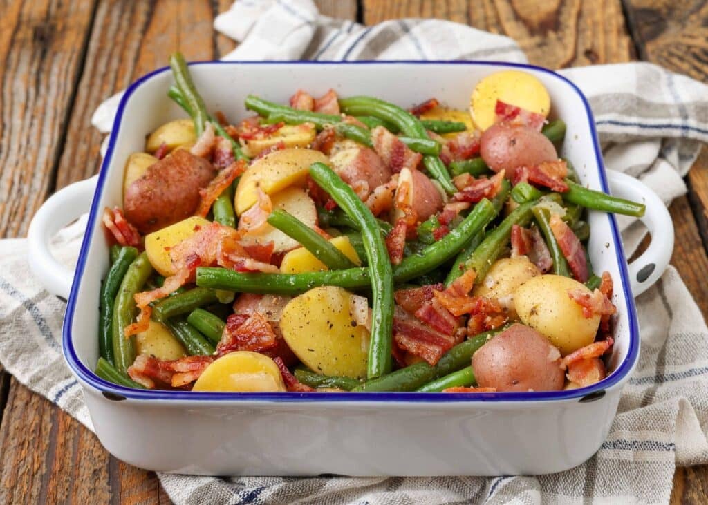 Green beans, potatoes, and bacon in white baking dish with blue rim