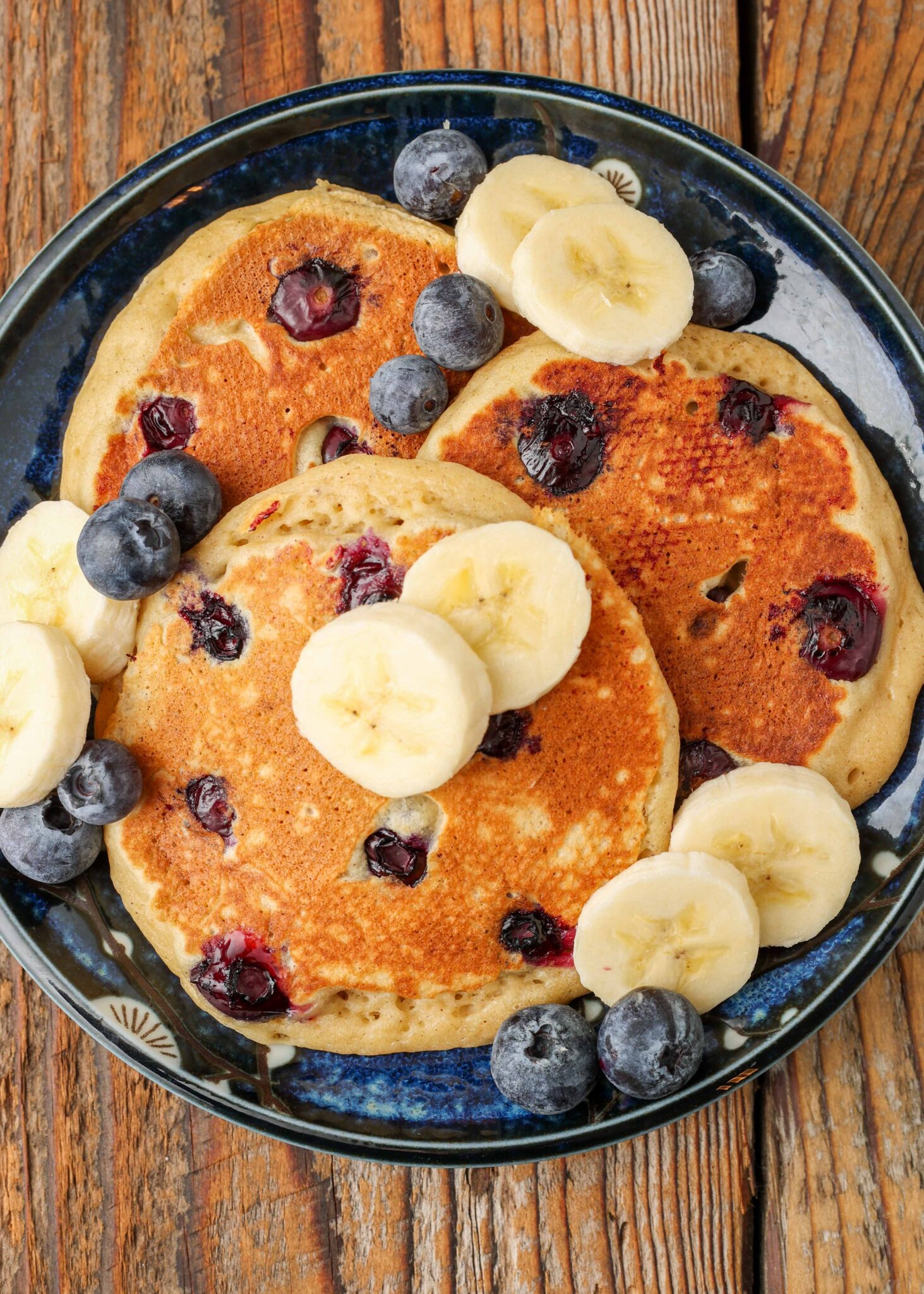 pancakes with sliced bananas and blueberries on plate on wooden table