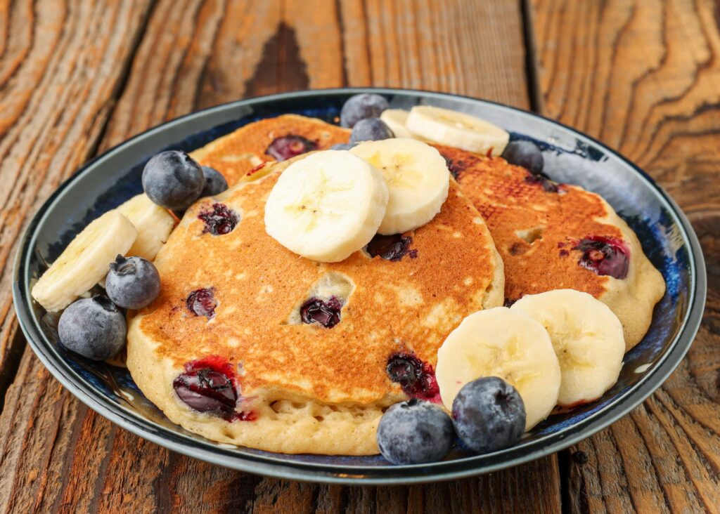 pancakes with bananas and blueberries on blue plate on wooden table