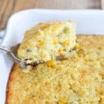 corn pudding with jalapenos in a white baking dish with serving spoon