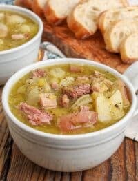 split pea soup with ham and potatoes in mugs with sliced bread next to them