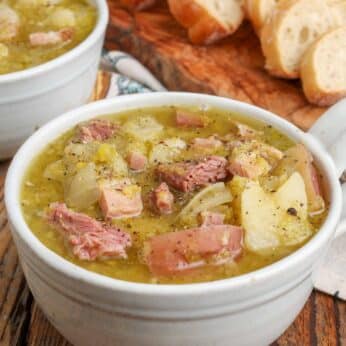 split pea soup with ham and potatoes in mugs with sliced bread next to them