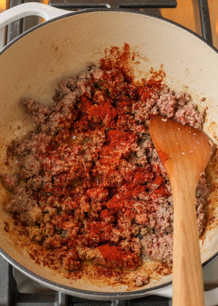 Sopa de repollo con carne molida y tomates en olla blanca con cuchara de madera. 