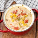 close up photos of chicken and corn soup in red crock with napkin