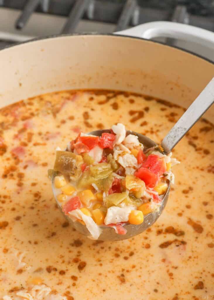 creamy chicken soup with corn and tomatoes in ladle in white pot