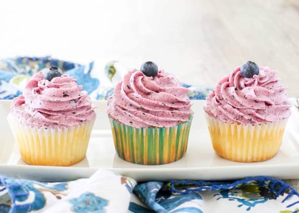 fresh blueberry frosting on white cupcakes on platter