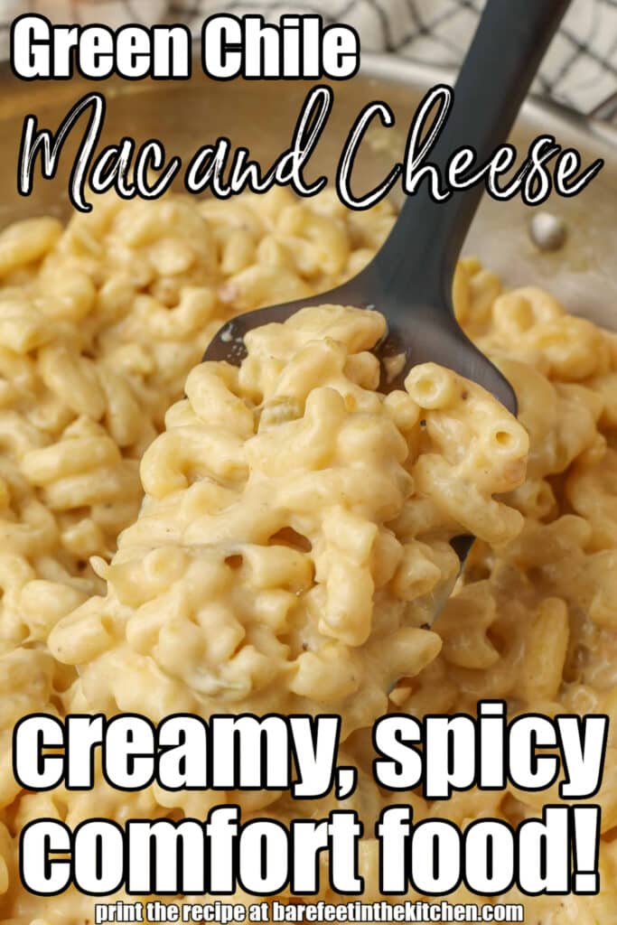 a black spoon lifts a serving of creamy mac and cheese with green chiles out of a metal skillet. white text is overlaid the image, reading "green chile mac and cheese, creamy, spice comfort food!"