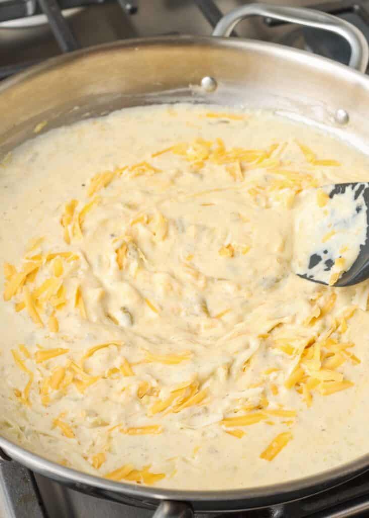 a process shot of mixing shredded cheese into the cream and spice mixture in a metal pan