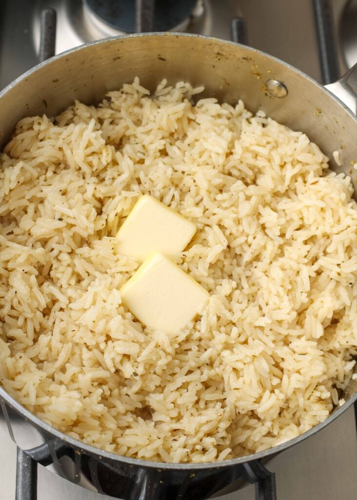 Overhead shot of jasmine rice and two melting pats of butter in stainless steel skillet
