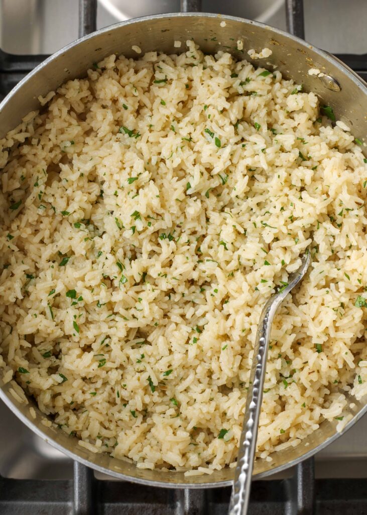 Fotografía cenital de arroz con hierbas italiano adornado con perejil en una olla de acero inoxidable con una cuchara de plata