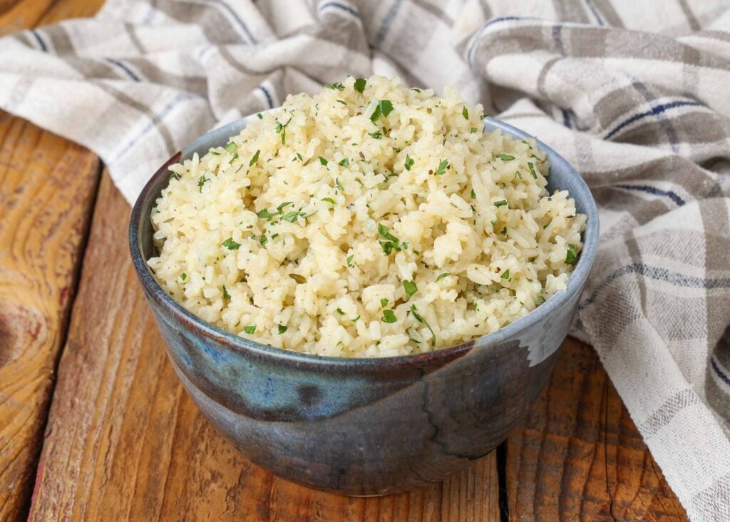 Buttery jasmine rice with herbs topped with parsley, served in a blue ceramic bowl with a checkered white and gray hand towel