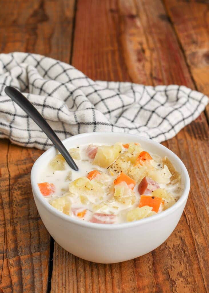 Zuppa di prosciutto e patate a cottura lenta in una ciotola monodose bianca con cucchiaio