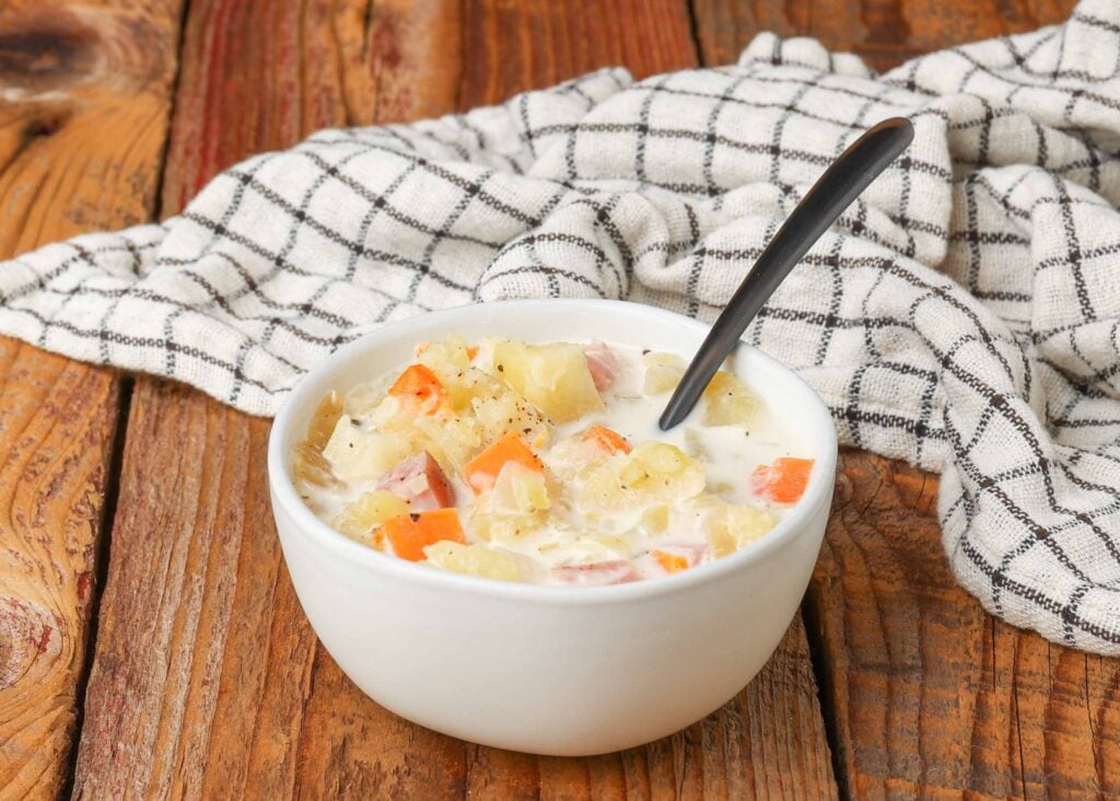 Put the ham and potato soup in the slow cooker into a white bowl and use a black spoon to