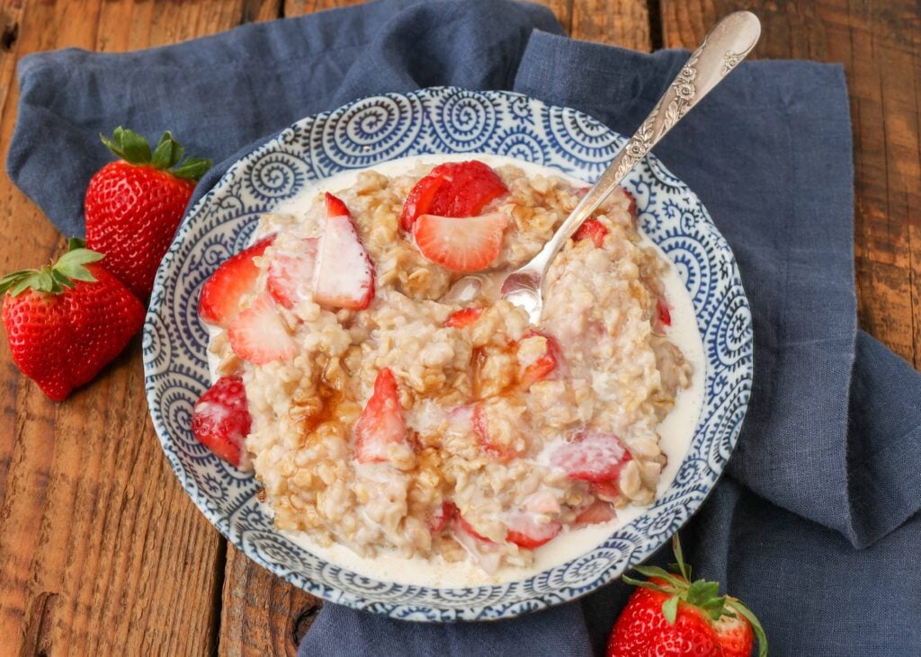 Oatmeal with strawberries and cream in blue bowl with spoon