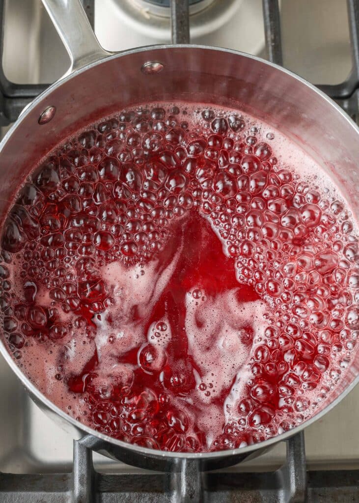 el jugo de fresa y el azúcar se combinan en una olla de metal en la estufa