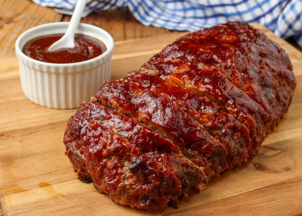 meatloaf with barbecue sauce on cutting board next to blue towel