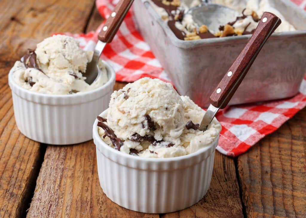 Two small bowls of banana ice cream with visible chunks of walnuts and chocolate each sport the wooden handle of a spoon sticking out