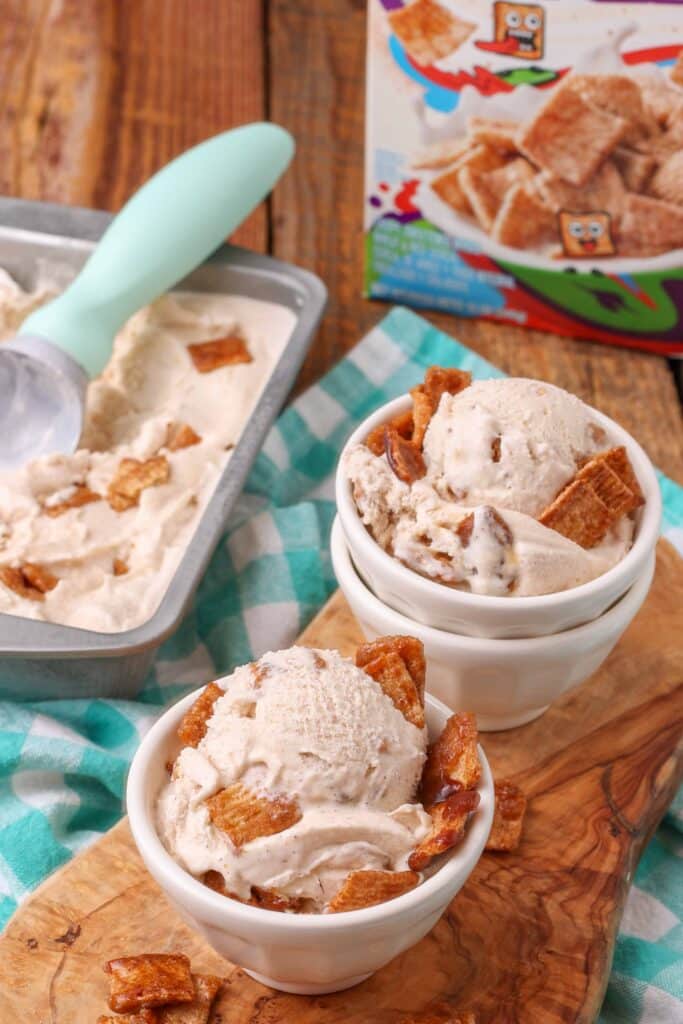 un tazón de helado y una tina de helado se ven en el fondo sobre una mesa de madera, cubierta con Cinnamon Toast Crunch