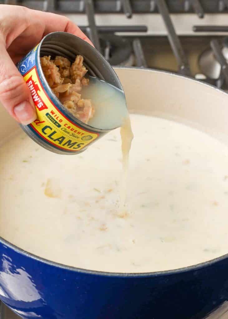 aggiungendo le vongole alla zuppa di pesce in una grande pentola blu