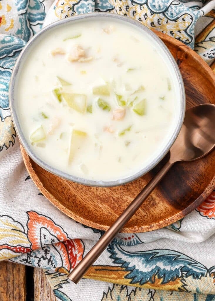 creamy chowder with clams and potatoes in bowl on wooden plate with spoon