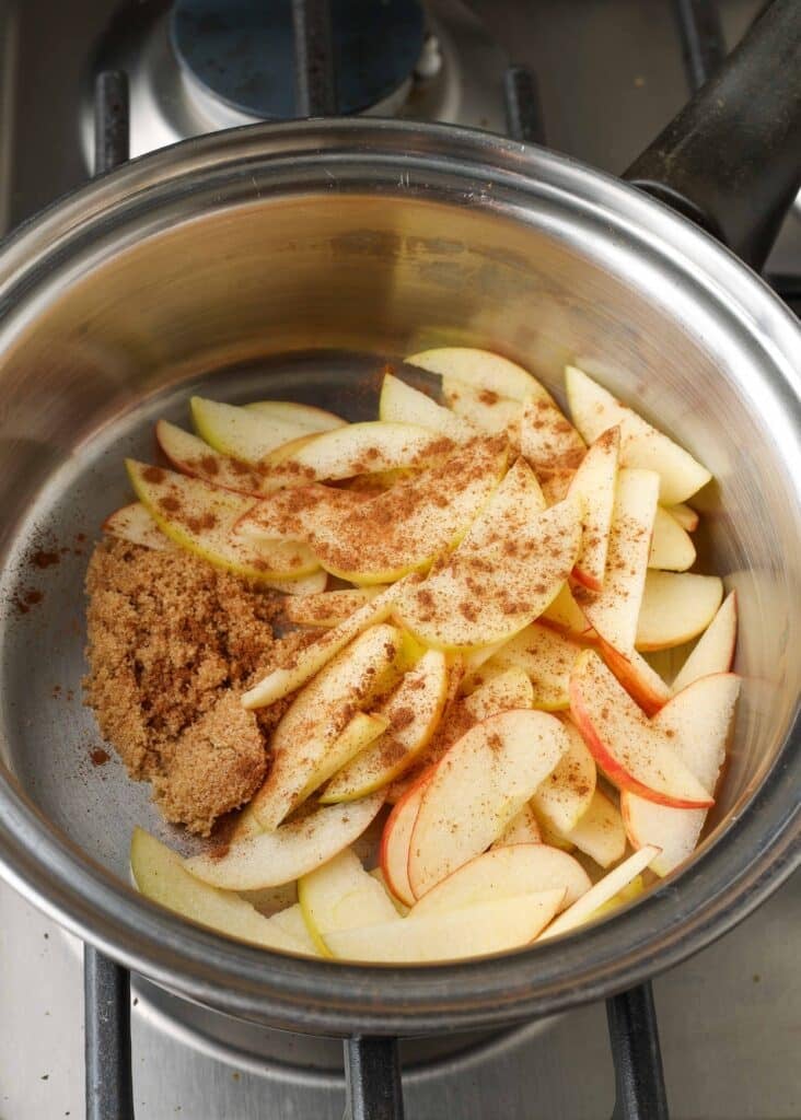 Manzanas en rodajas finas con piel roja sazonadas y listas para cocinar en una olla pequeña de metal