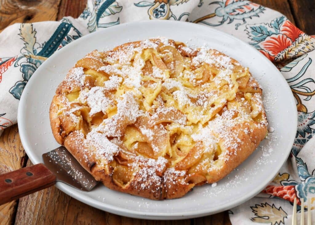 a photo of a german pancake on a white plate with a colorful napkin in the background