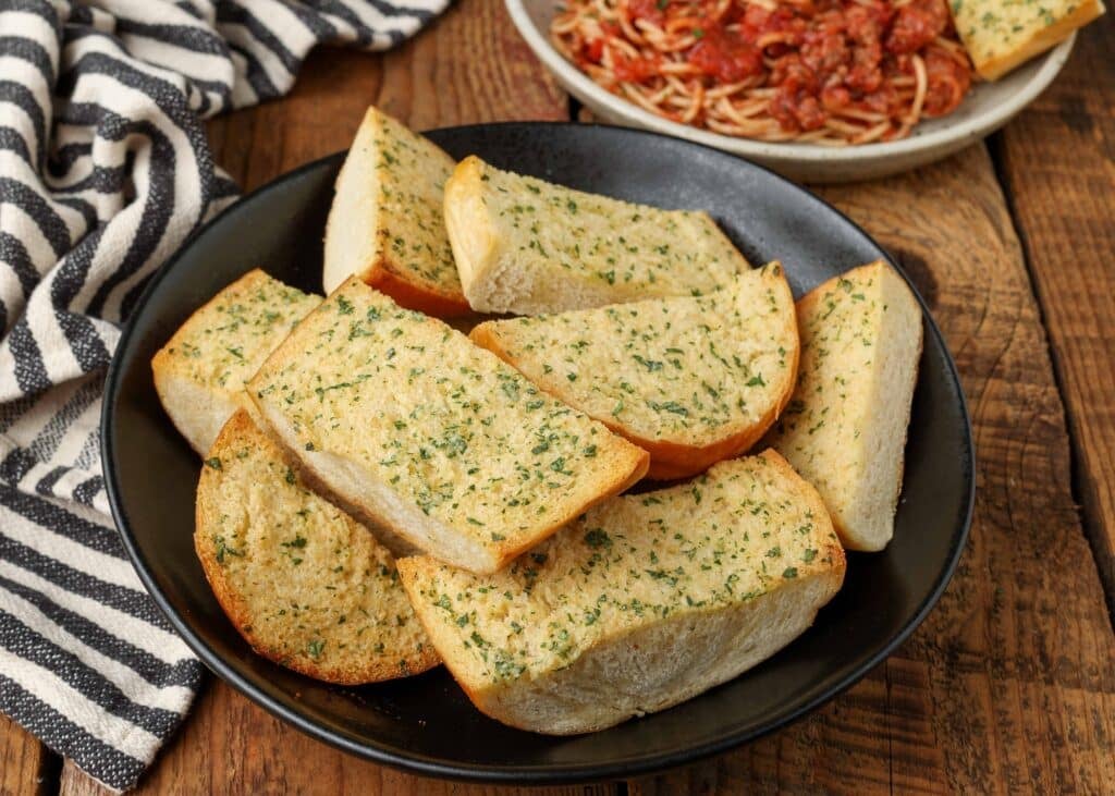 garlic bread with herbs in black bowl on wooden table