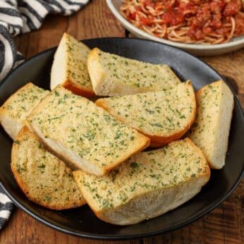 garlic bread with herbs in black bowl on wooden table