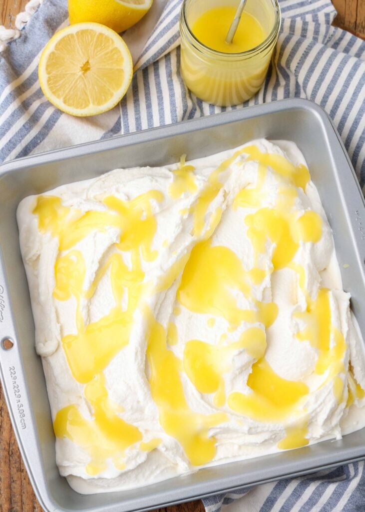 A metal pan full of ice cream sprinkled with lemon curd rests on a blue and white striped tea towel