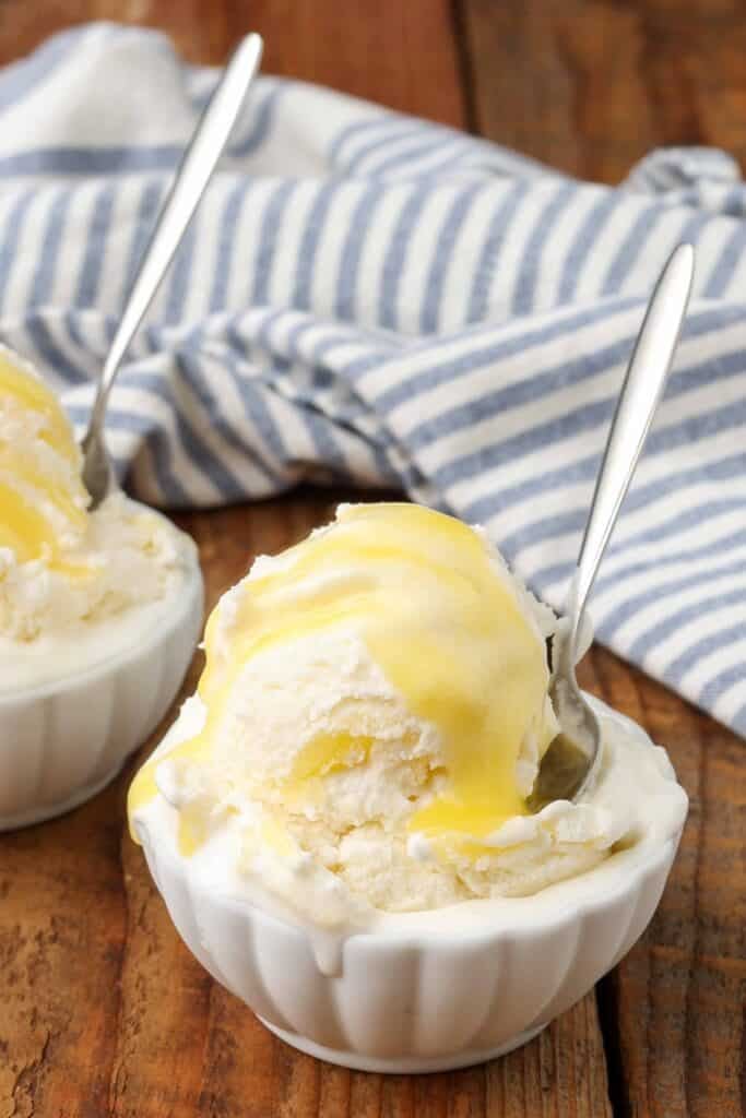 Una bola de helado de cuajada de limón se sienta en un pequeño tazón blanco con una cuchara de metal de mango largo que sobresale