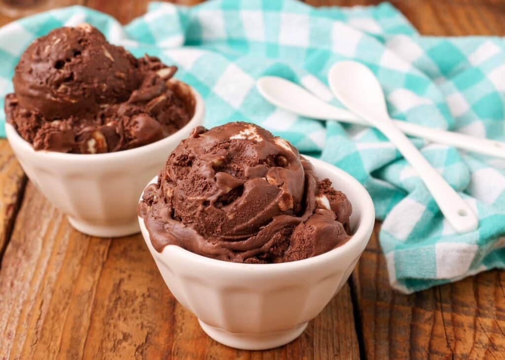 helado de chocolate con almendras y malvaviscos en un tazón blanco pequeño con una cuchara
