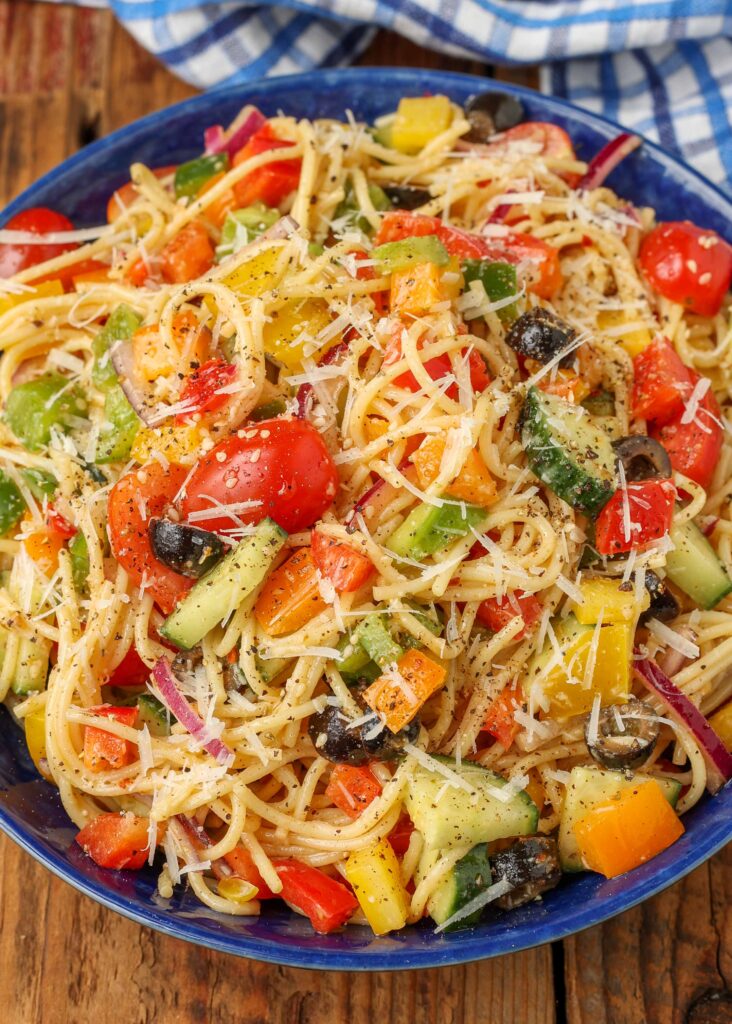 A close up photo of a bowl of spaghetti salad with vegetables and shredded parmesan