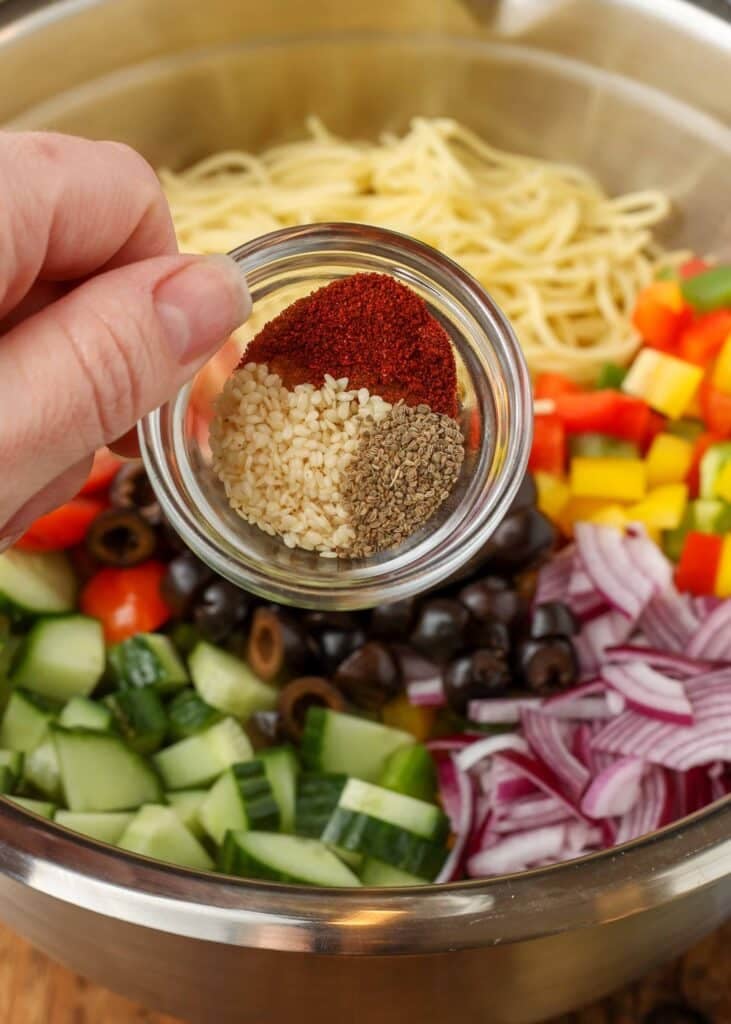 A close-up photo of the spices in a tiny glass bowl with the other ingredients visible in the background in a metal bowl