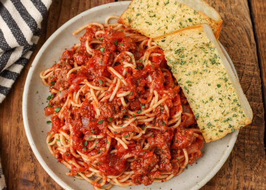 un piatto bianco carico di spaghetti alla bolognese e due fette di pane all'aglio
