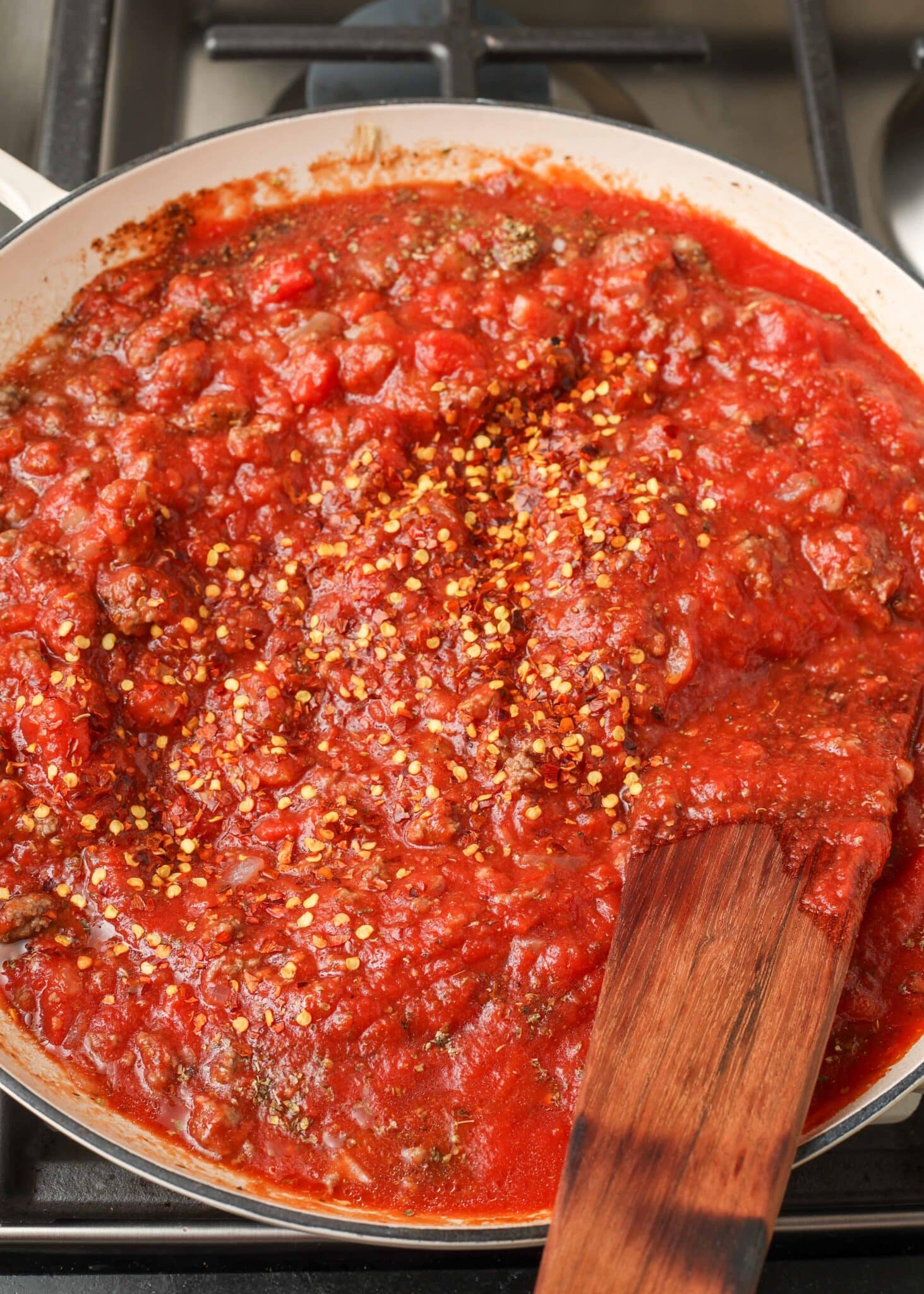 Finished spaghetti sauce with ground beef simmers in a white skillet with a wooden spatula